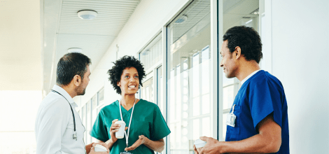 Three medical professionals talking during coffee break in hospital corridor